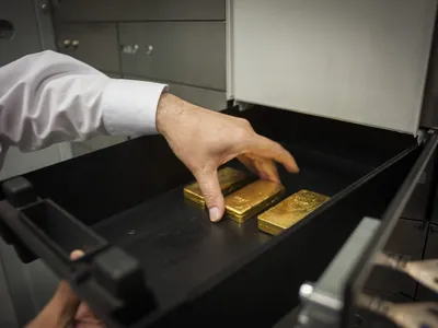 A hand retrieving gold bars from a vault safe-deposit box