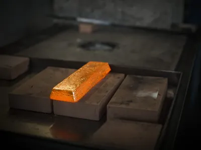 A glowing gold bar held with tongs, ready for quenching