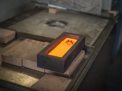 A glowing gold bar resting on firebrick after leaving the mould