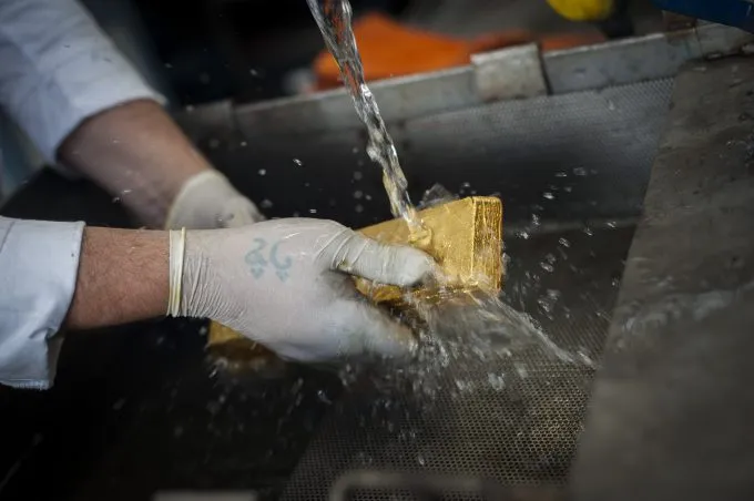 Gloved hands rinsing a freshly cast gold bar under running water at the Sharjah refinery