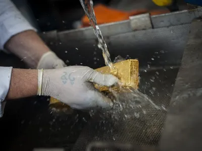 A finished gold bar being rinsed clean under running water